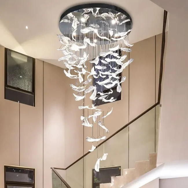 Intricate glass feather chandelier with cascading translucent feathers hangs in a modern space, creating an artistic, ambient glow against a blue-toned window background.