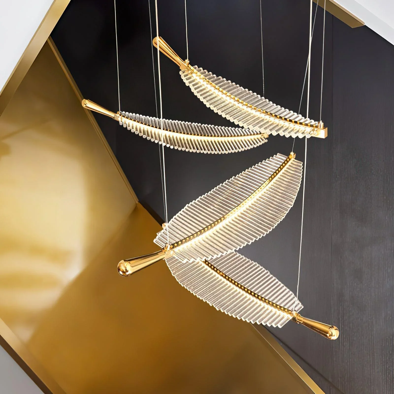 A modern artistic chandelier with four feather-like lights, transparent strips and gold metal details, emitting warm light, creating a luxurious and stylish ambiance.